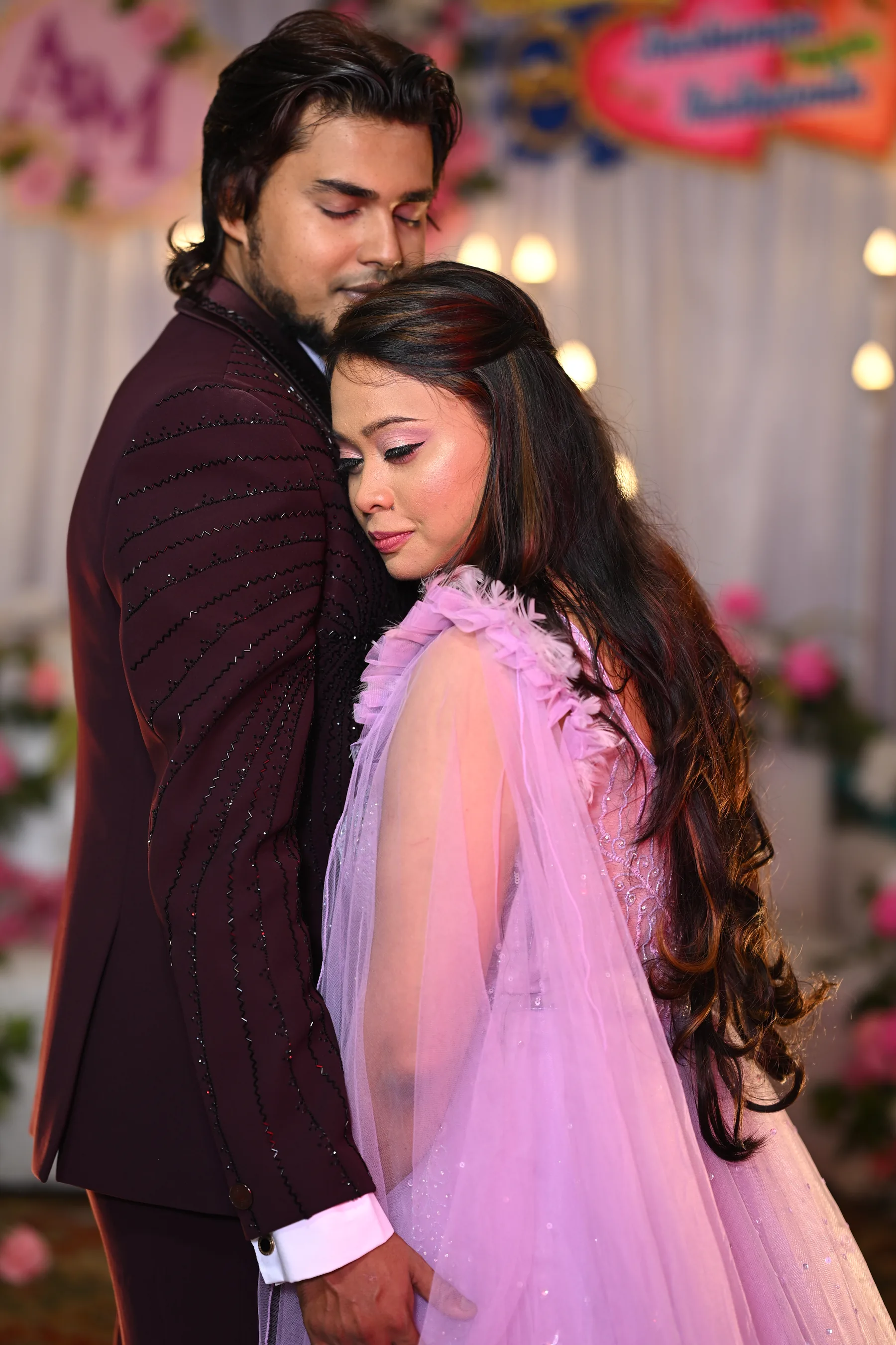 Engaged couple embracing in front of a floral backdrop
